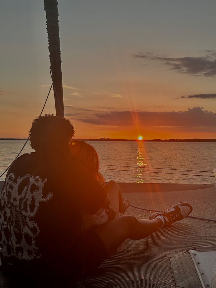 a person sitting on the deck of a boat watching the sun go down over the water