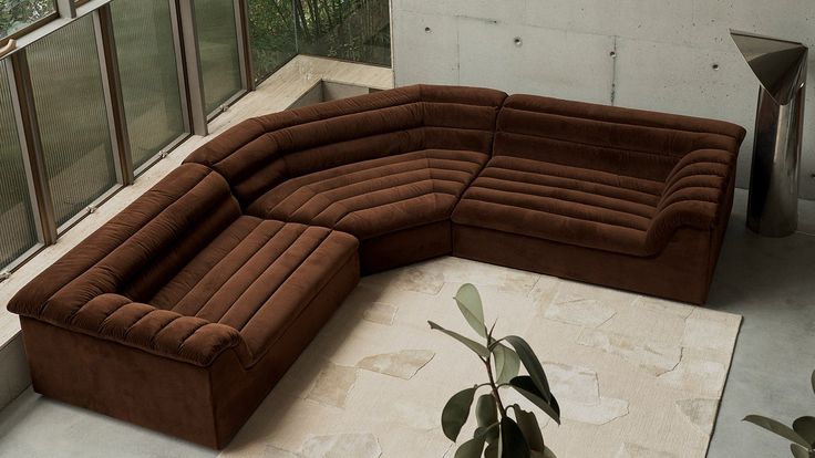 a large brown couch sitting on top of a white rug next to a tall window