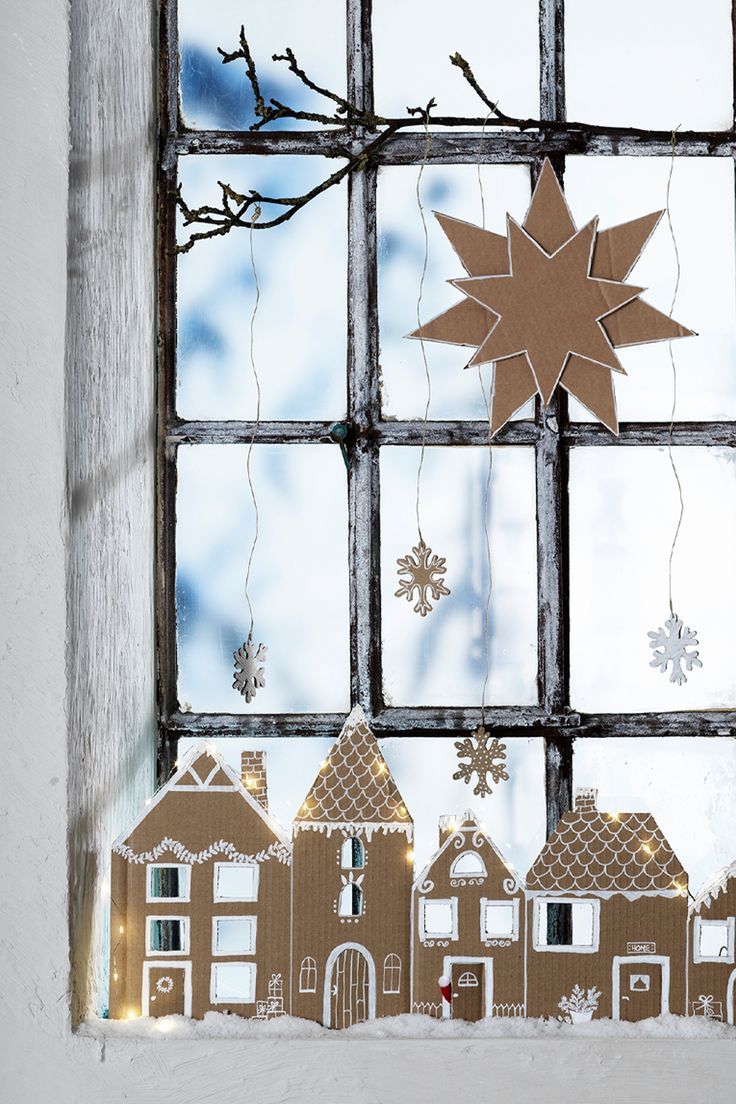 a paper cut out of a house with snowflakes hanging from the windowsill