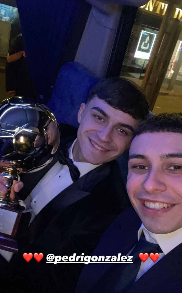 two men in tuxedos pose for the camera with an award on their chest