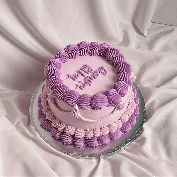 a pink and purple birthday cake sitting on top of a white sheet covered tablecloth