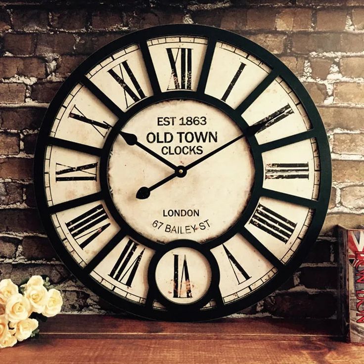 an old town clock sits on a shelf next to some flowers and a brick wall