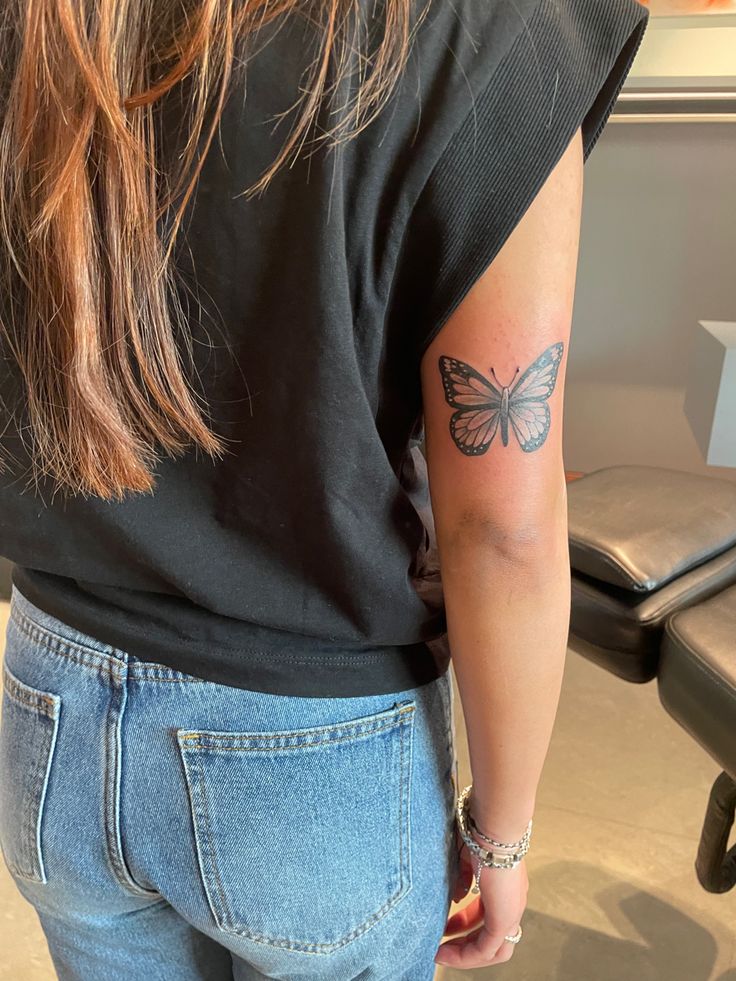 a woman with a butterfly tattoo on her left upper arm and right lower arm behind her back