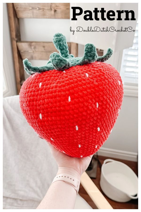 a hand holding up a knitted strawberry pillow