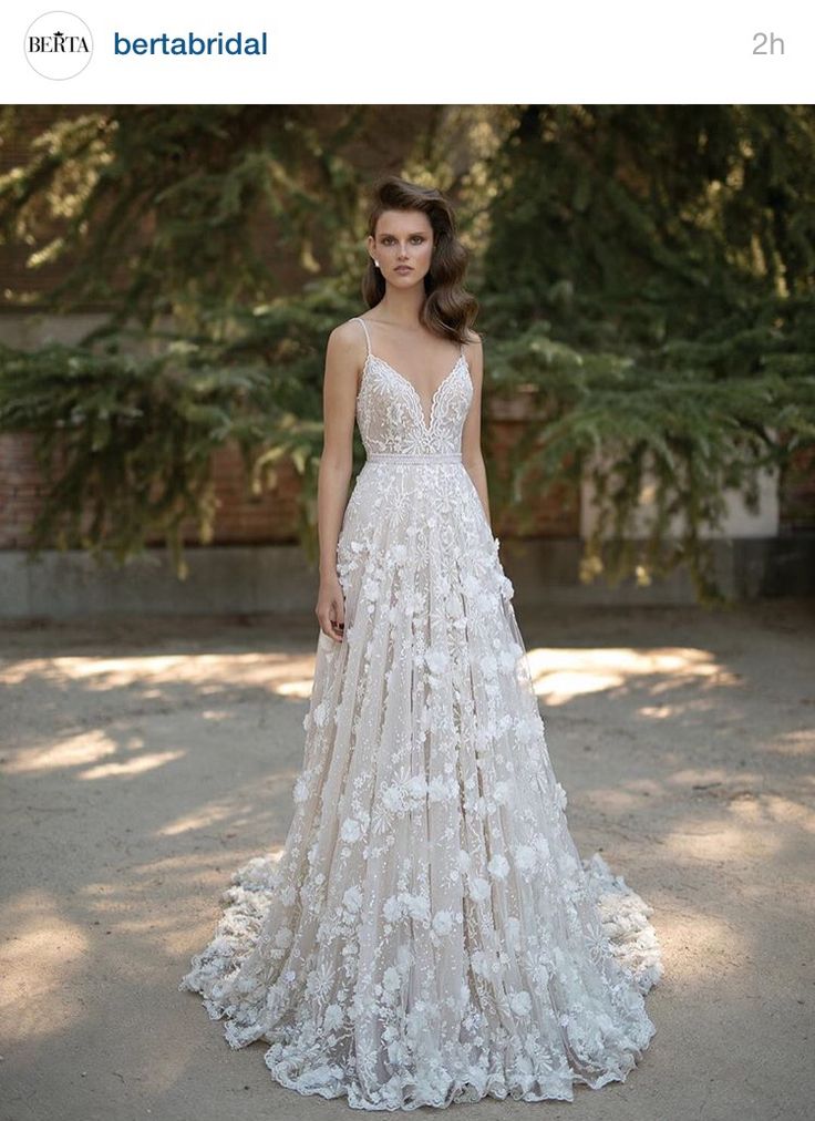 a woman in a white wedding dress standing on the street with trees behind her and looking at the camera