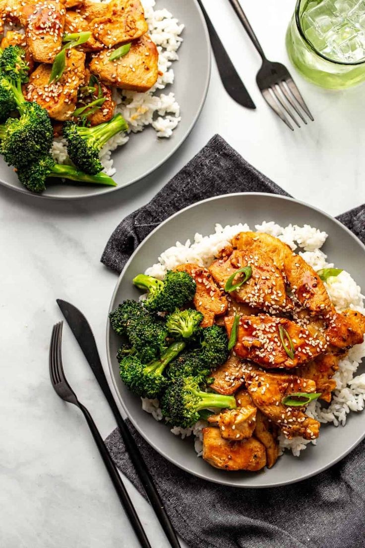 two plates with chicken, broccoli and rice on them next to silverware