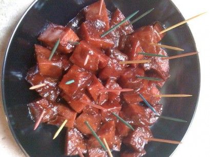 a black plate topped with meat and toothpicks on top of a white table