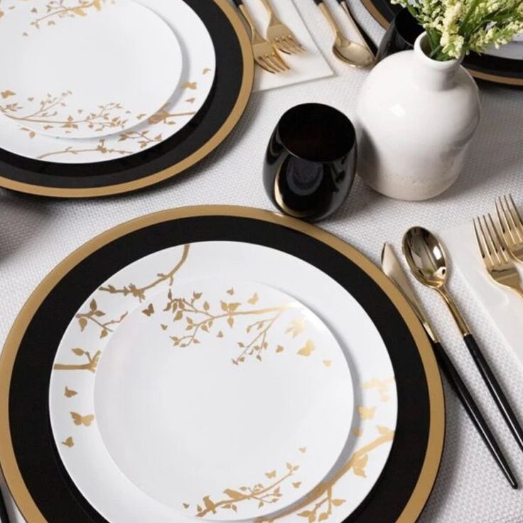 the table is set with black and gold place settings, silverware, and flowers