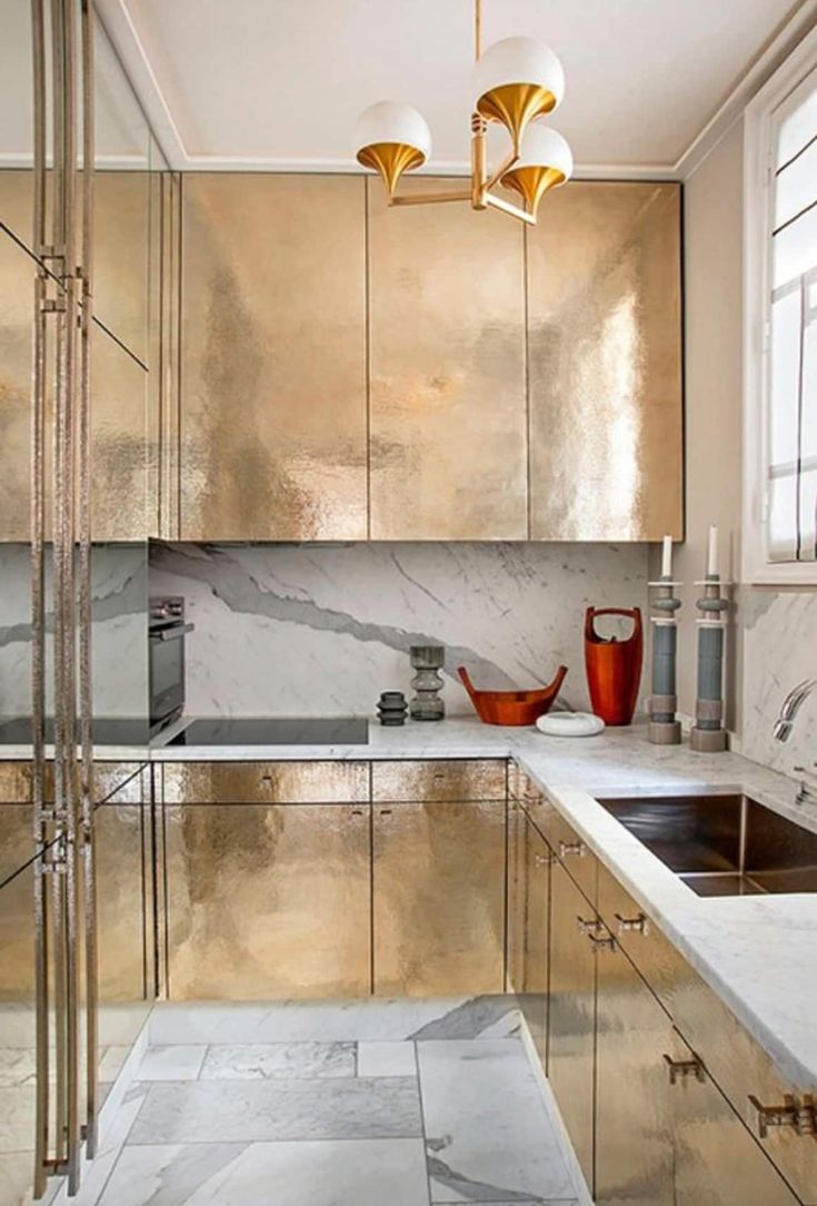 a kitchen with gold cabinets and marble counter tops in the center, along with two hanging lights over the sink