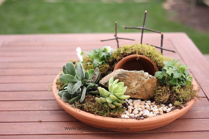 a potted planter with rocks and succulents on a wooden table