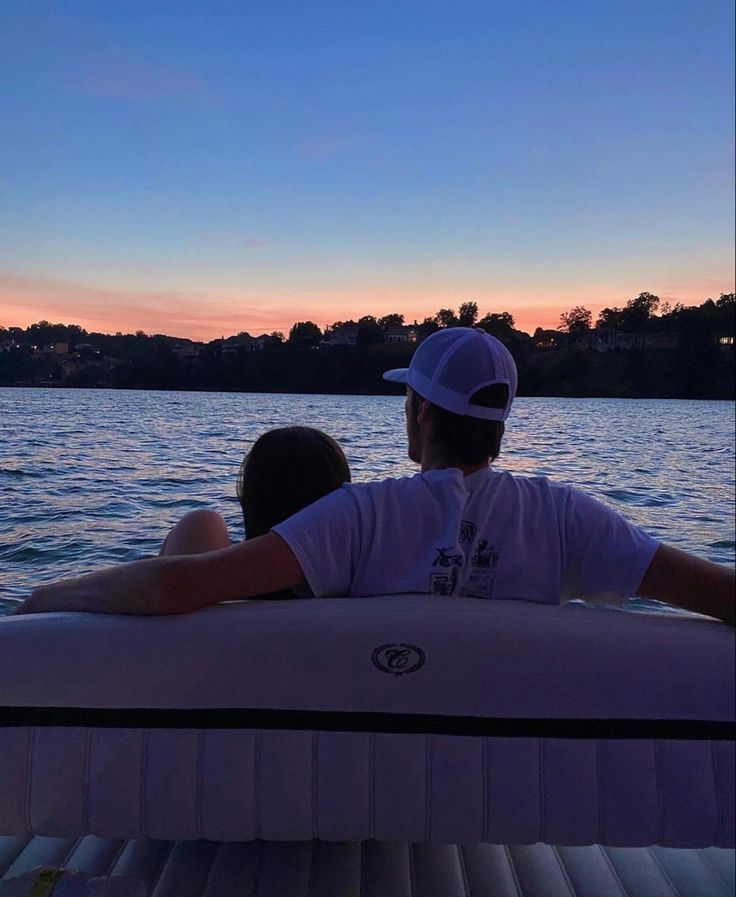 two people sitting on top of a boat in the water at sunset or sunrise time