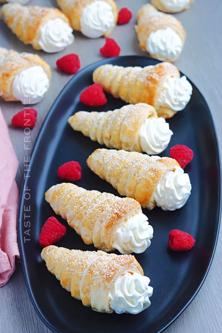 small pastries with whipped cream and raspberries on a black plate