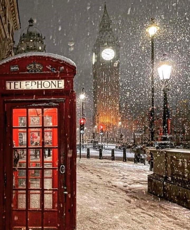 a red phone booth sitting in the middle of a snow covered street next to a clock tower