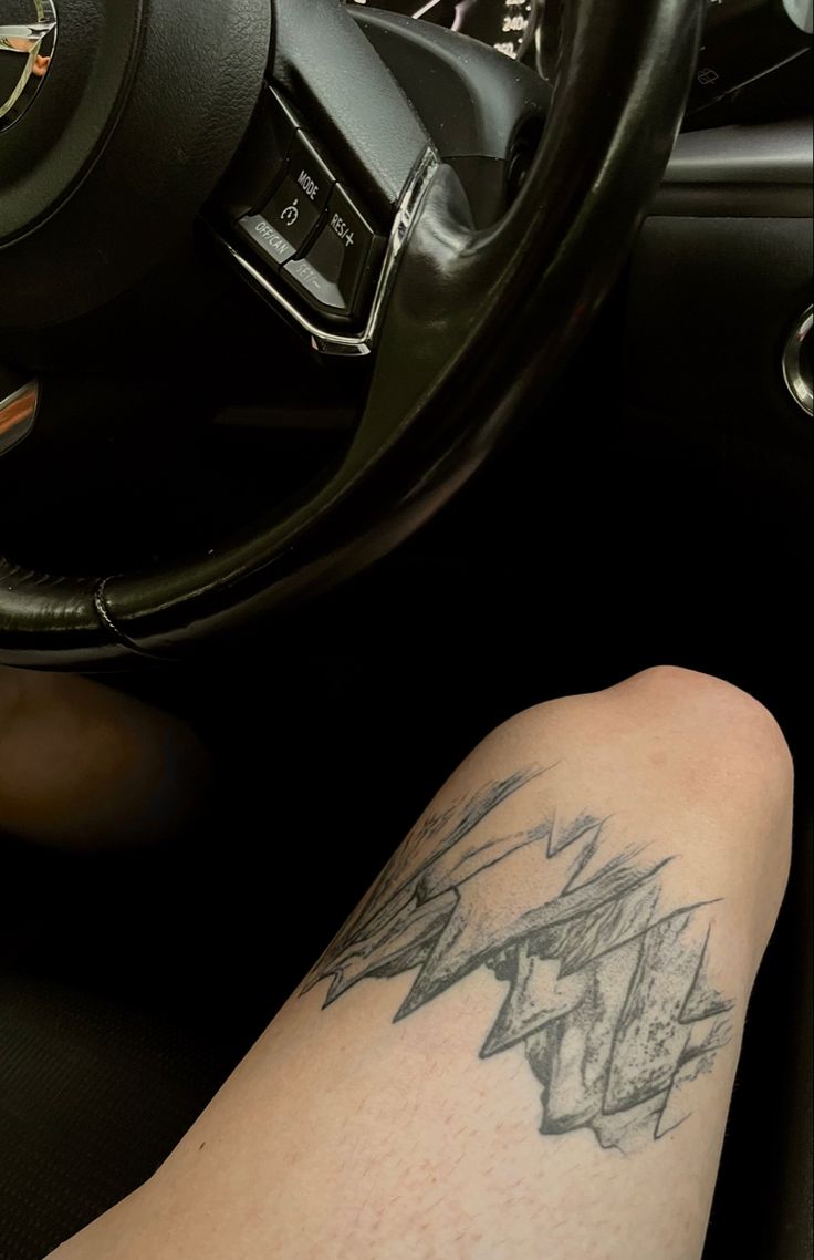 a person with a tattoo on their arm sitting in a car next to a steering wheel