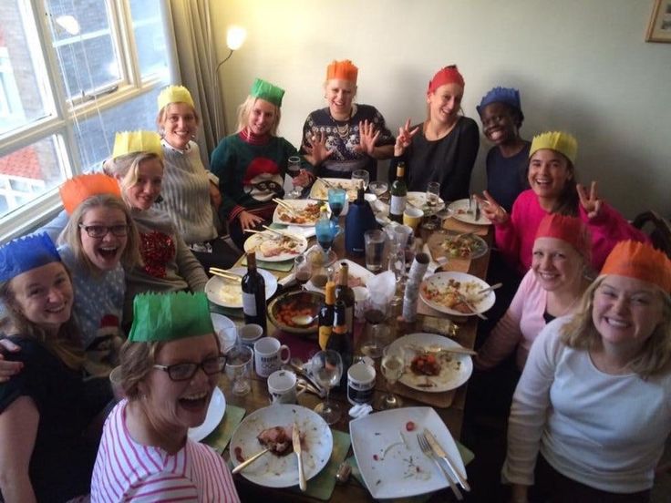 a group of people sitting around a table with plates of food on it and wearing party hats