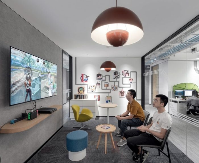 two men sitting in chairs watching television in an office setting with large screens on the wall