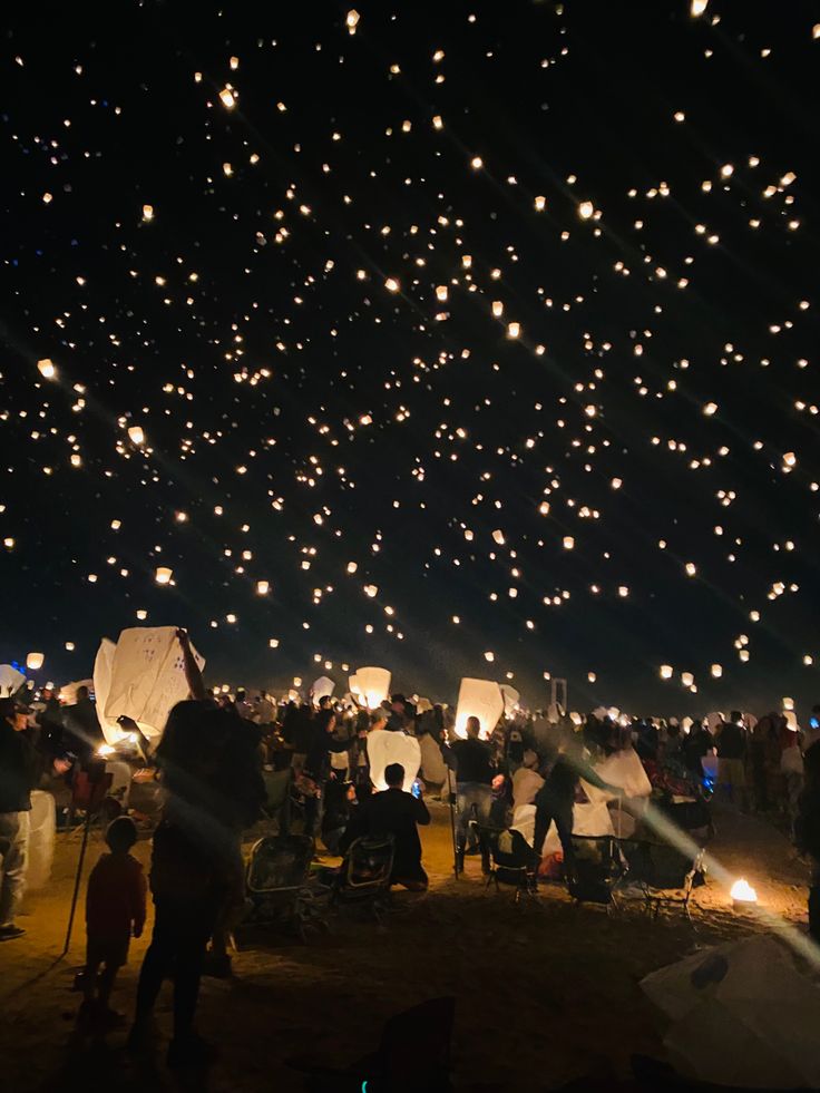 the sky is filled with lots of balloons and people are gathered around them at night