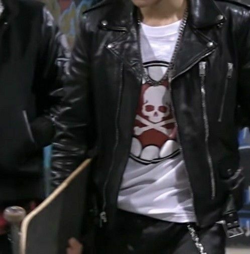 a man wearing a skull t - shirt and black leather jacket walking down the street