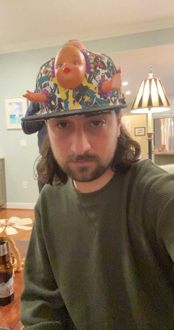 a man sitting at a table with a beer in front of him and a toy pig on top of his hat