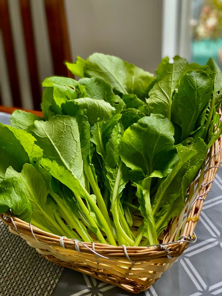 a basket filled with green leafy greens on top of a table