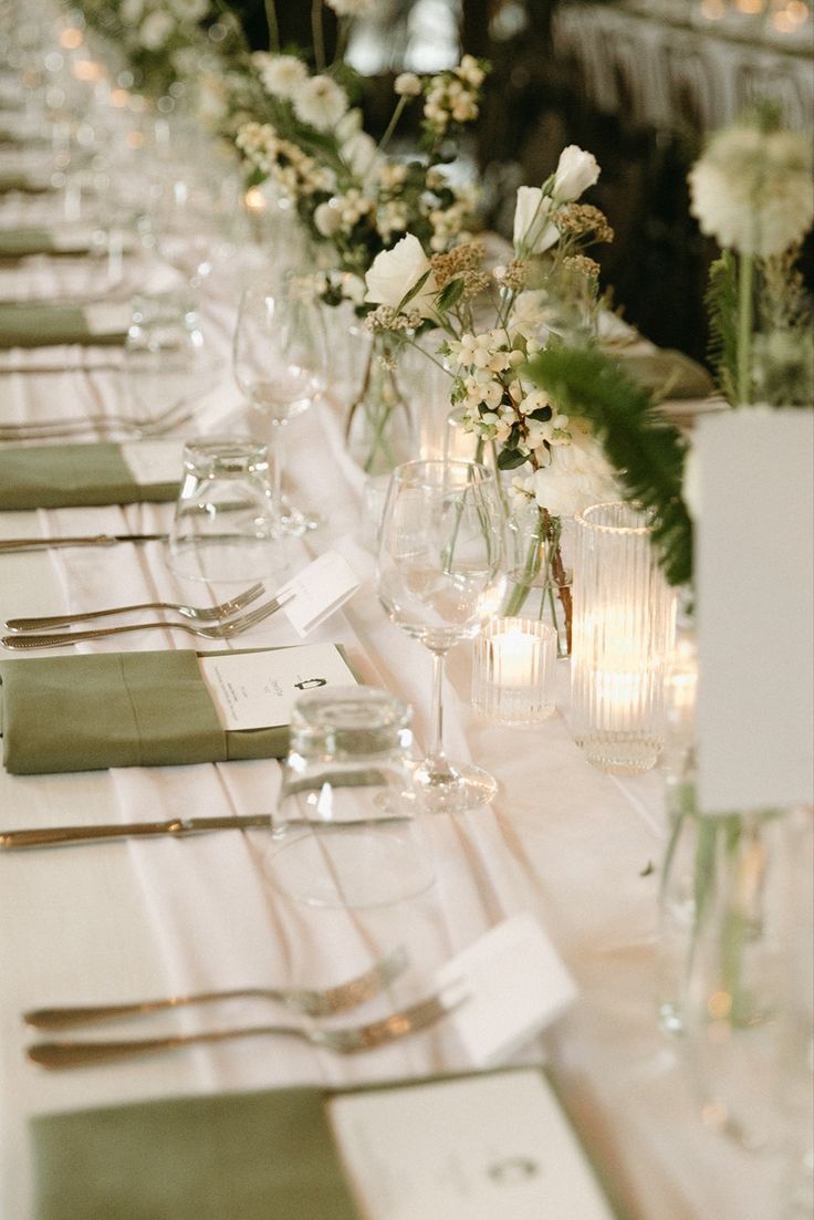 a long table is set with place settings and flowers in vases on each side