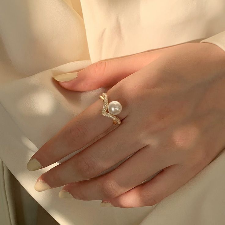 Romantic gold pearl ring A lustrous pearl sits on the diamond v shape band, just like a pearl sun rising from the diamond waves. It is easy to tell the romantic tone and elegant style of the v-shaped ring at the first glance. High-quality 7-8mm faux pearl decorate with sparkling diamonds, no one can move their eyes from your hand with the pearl ring gold. The adjustable design makes the pearl diamond ring suitable for most women. V shaped pearl ring gold for elegant style Inlaid with many diamon Pearl Rings In Gold, Pearl Ring Design, Pearl Ring Gold, Pearl Jewelry Ring, Pearl Diamond Ring, Pearl Wedding Ring, Sun Rising, Pearl Jewelry Design, Pearl Engagement Ring