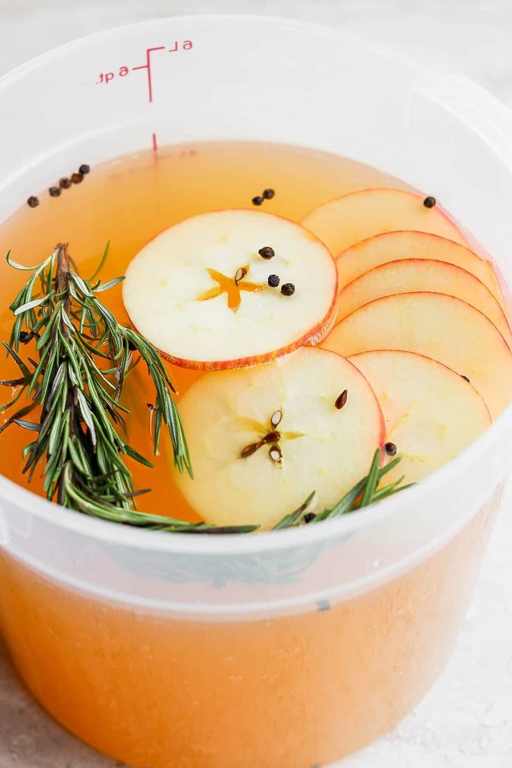 apples and rosemary are in a bowl on the table with an orange liquid, salt and pepper for garnish