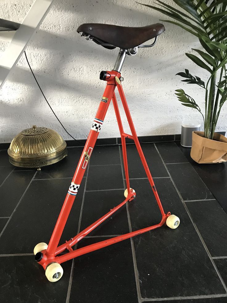 a red bicycle stand sitting on top of a black tile floor next to a potted plant