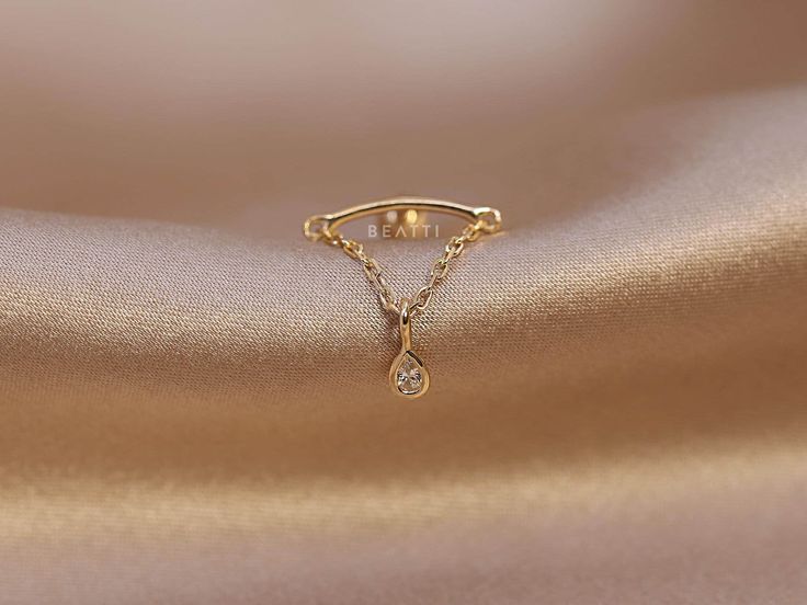 a gold ring with a diamond hanging from it's side on a satin surface