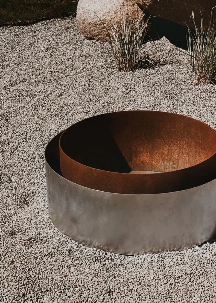 a large metal bowl sitting on top of a gravel covered ground next to a rock