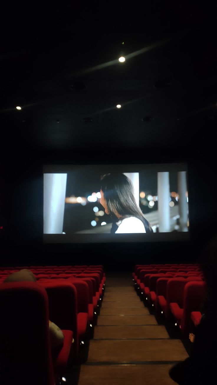 an empty auditorium with red seats and a large screen on the wall, showing a woman's profile