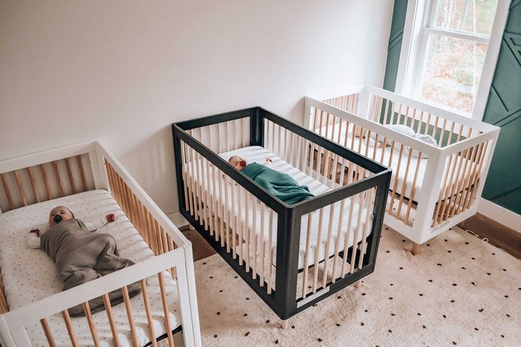 two cribs in the corner of a room, one with a sleeping baby