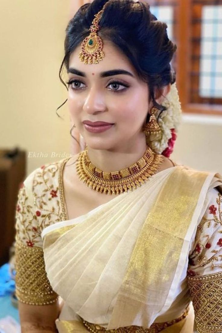 a woman in a white and gold sari with jewelry on her neck, posing for the camera