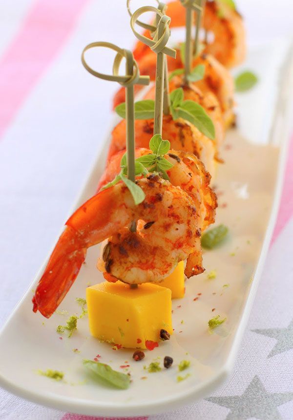 a long white plate topped with shrimp and cheese on top of a striped table cloth