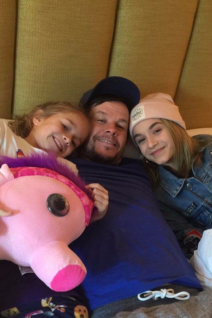 a man, woman and child laying on a bed with a stuffed animal in front of them