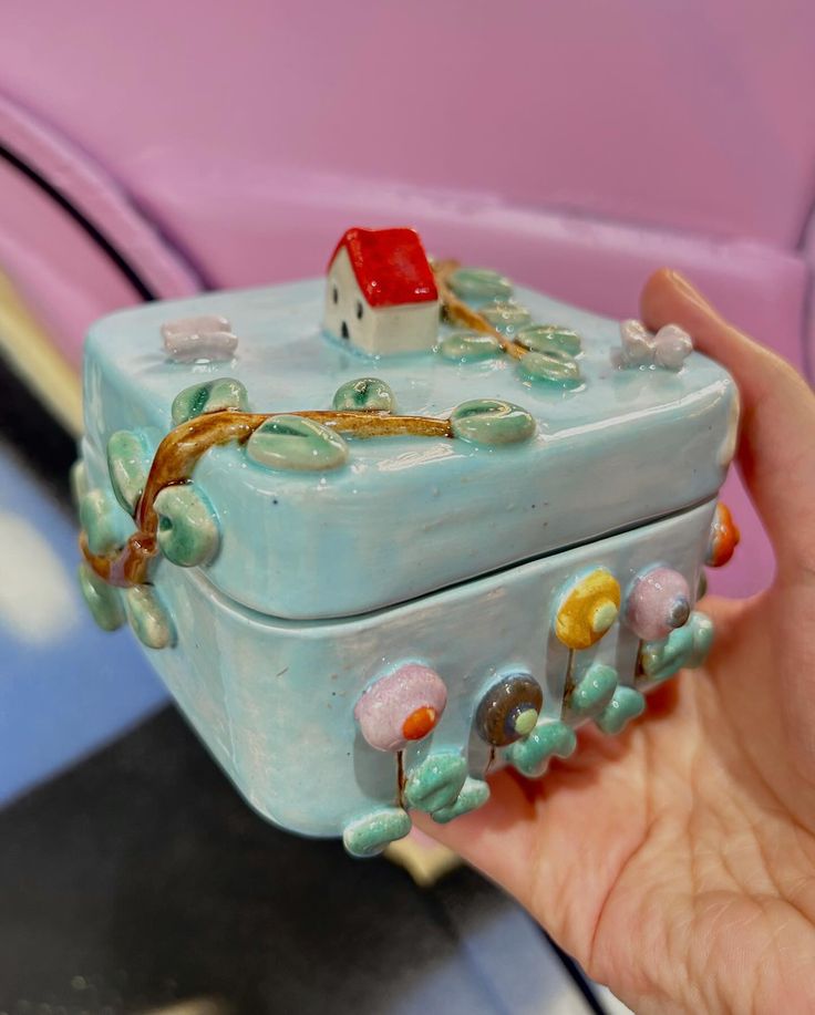 a hand holding a small blue box with a red house on it's lid