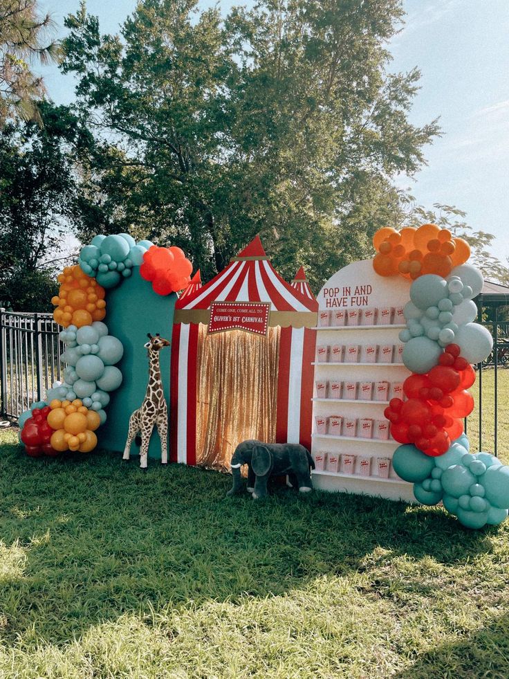 a circus tent with balloons and giraffes on the grass in front of it