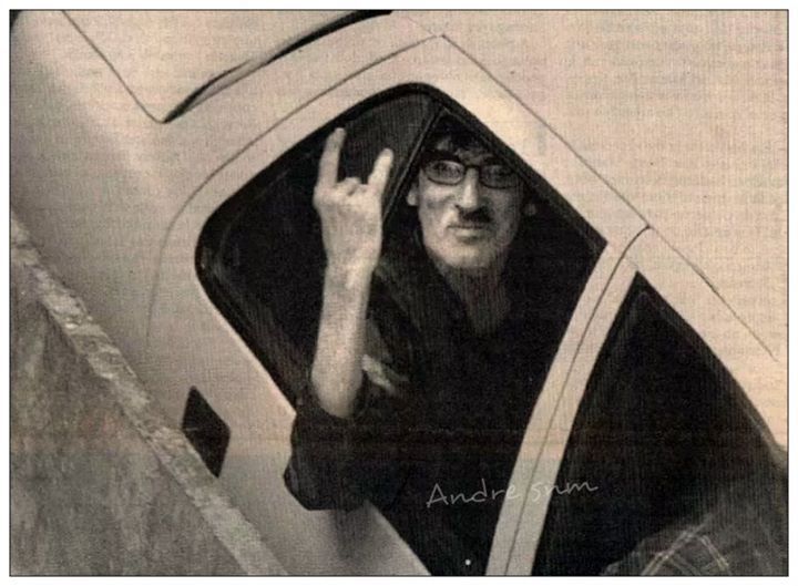 a man sitting in the passenger seat of a car with his hand up and pointing at something