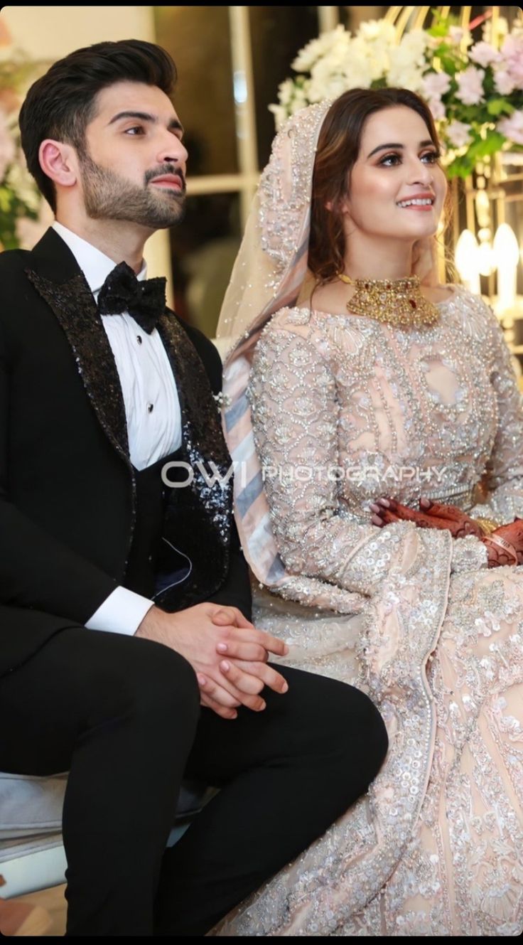 a man and woman sitting next to each other in formal wear, posing for the camera