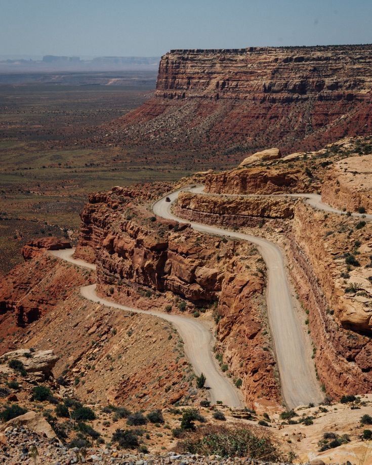 a winding road in the middle of an arid area with red rocks and green plants