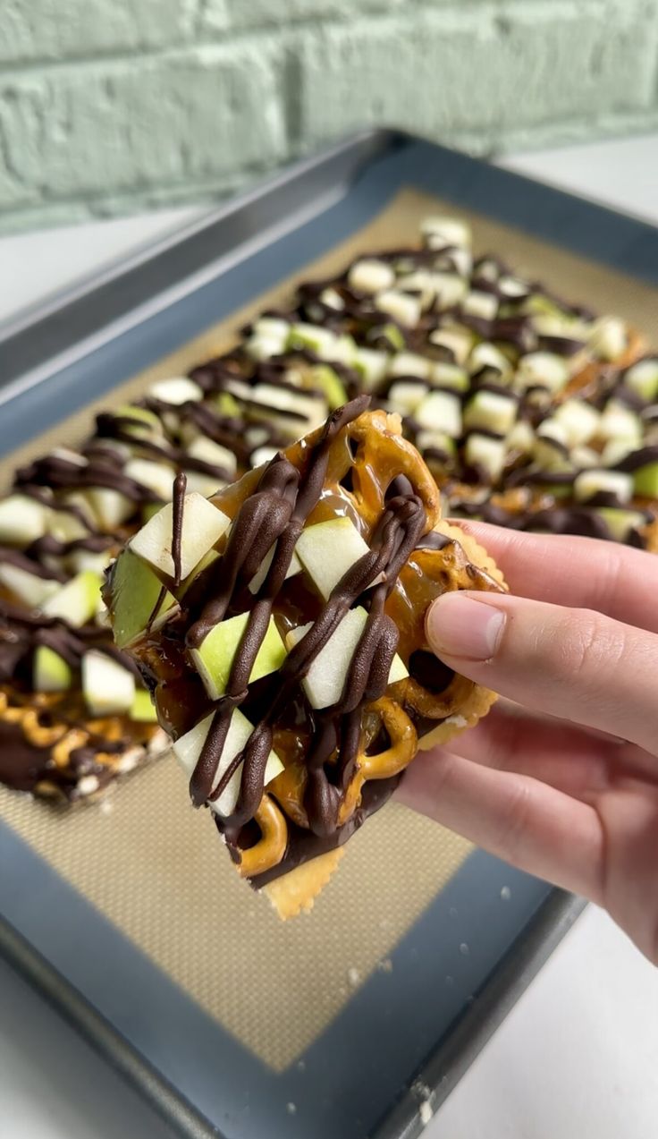 a person holding up a piece of food with chocolate and apple toppings on it