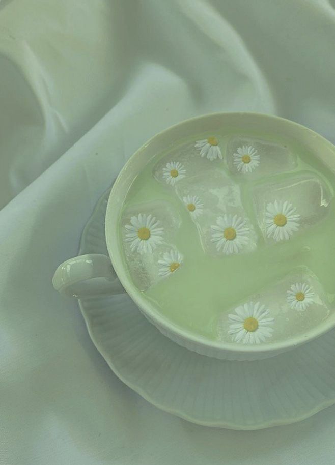 a cup filled with water and daisies on top of a white cloth covered table