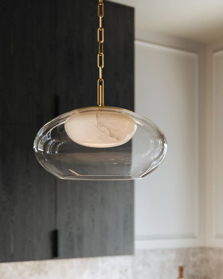 a glass light fixture hanging from a ceiling in a kitchen with marble counter tops and cabinets