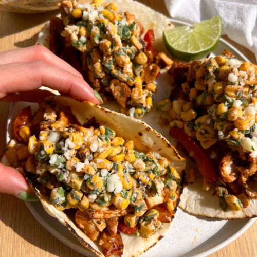 a plate with three tacos on it and someone reaching for the tortilla