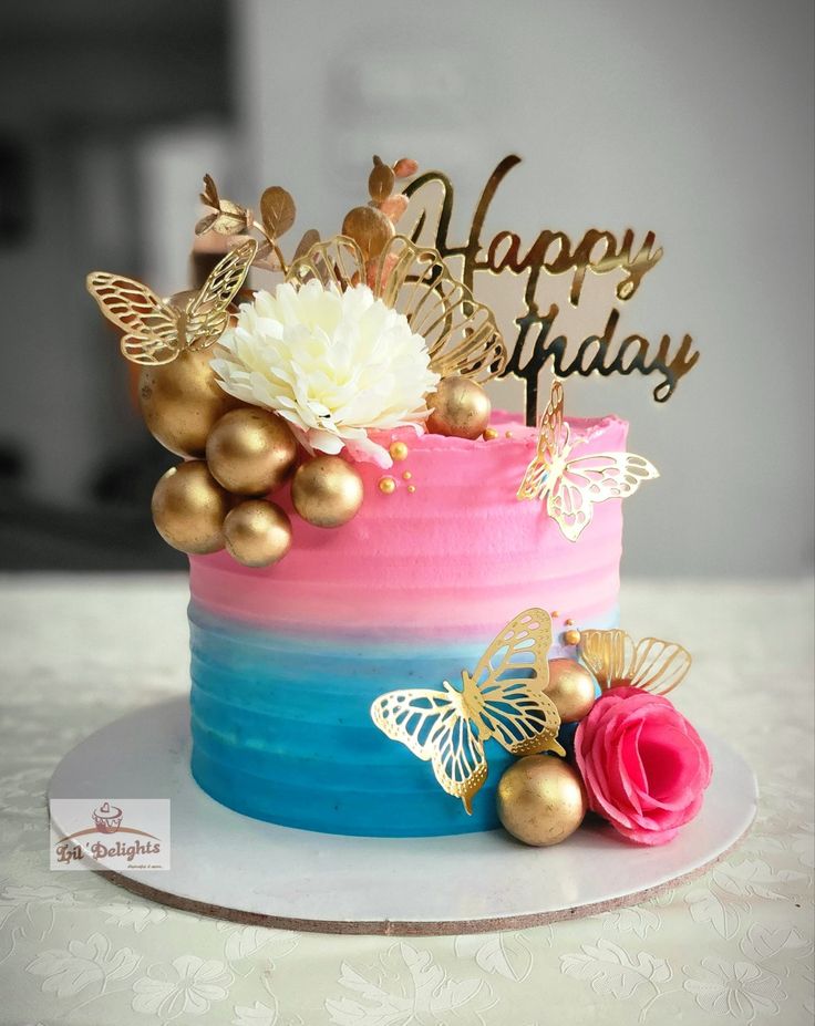 a birthday cake decorated with gold and pink frosting, topped with flowers and butterflies