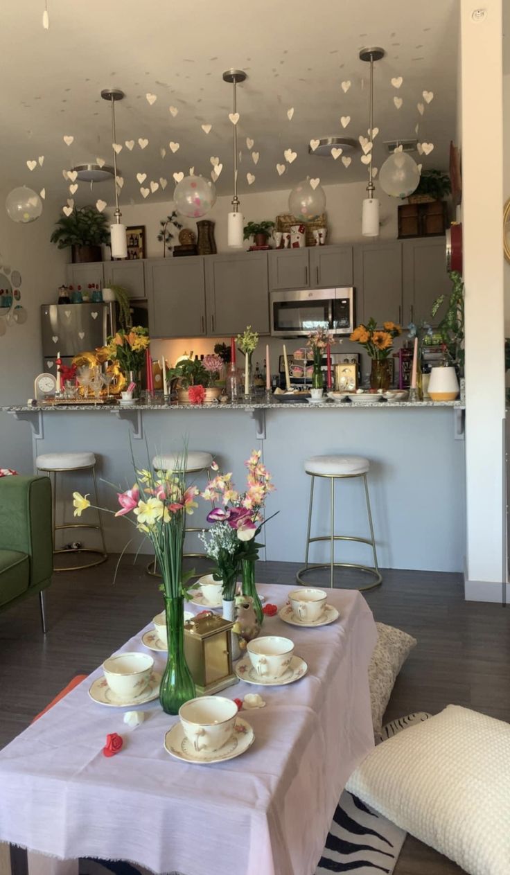 a table with plates and cups on it in front of a kitchen counter filled with flowers