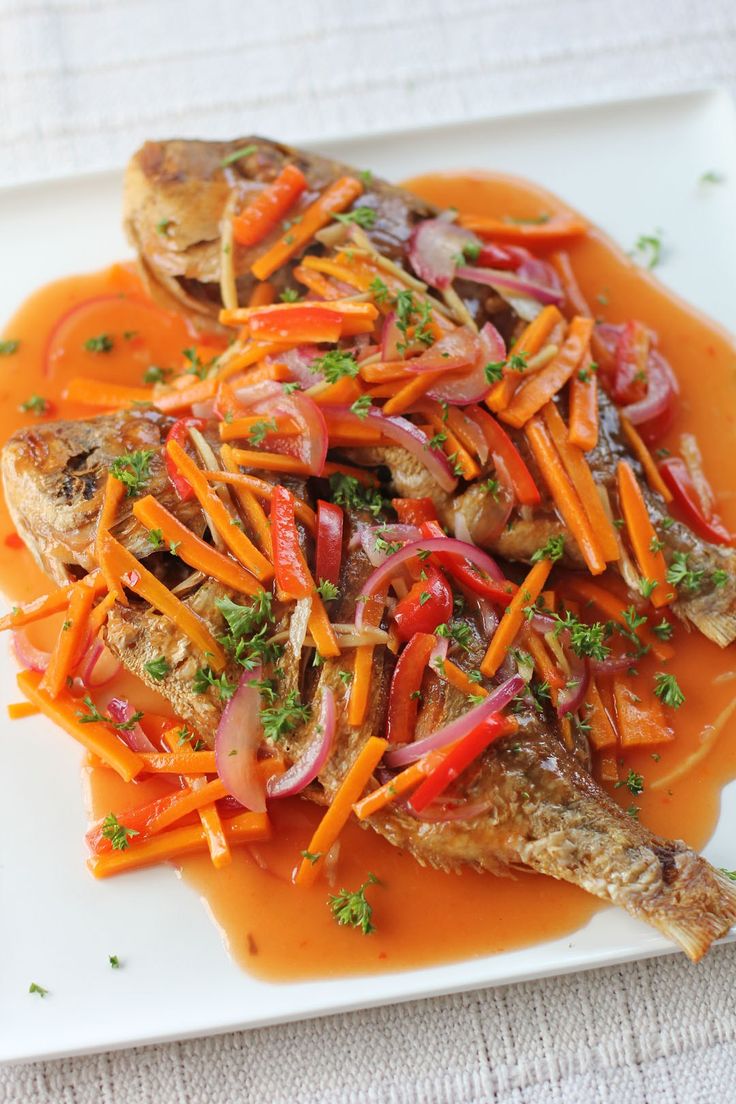 a white plate topped with fish covered in carrots and gravy on top of a table