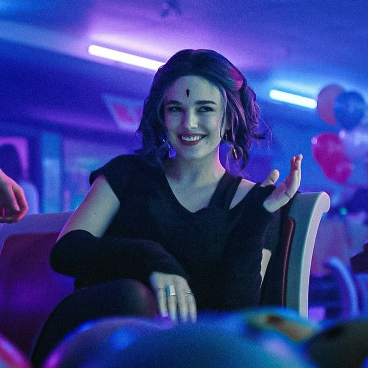 a woman sitting in a chair with her hands up and smiling at the camera while balloons are floating behind her