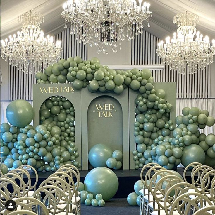 a room filled with lots of chairs covered in blue and green balloons next to a chandelier