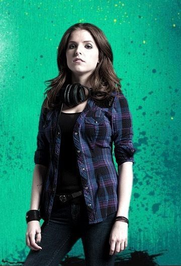 a woman standing in front of a green wall wearing a black shirt and jeans with her hands on her hips